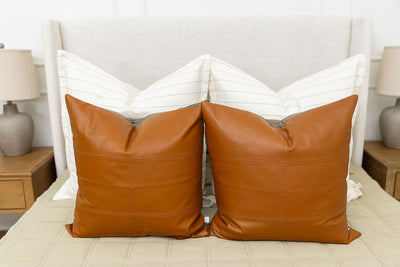 A bed with cream striped XL euro pillows and leather euro pillows arranged on a bed made with green zipper bedding