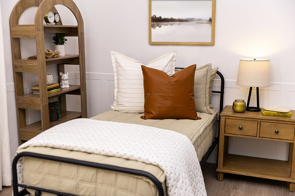 A twin bed with green zipper bedding and an assortment of cream and leather bedding accessories.