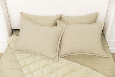 A bed made with khaki green zipper bedding, the top portion unzipped and pulled back, with four pillows arranged on top of the bed.