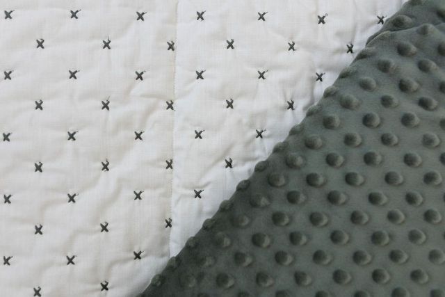 A dual sided blanket, one side with minky and the other side cream with gray x pattern stitching