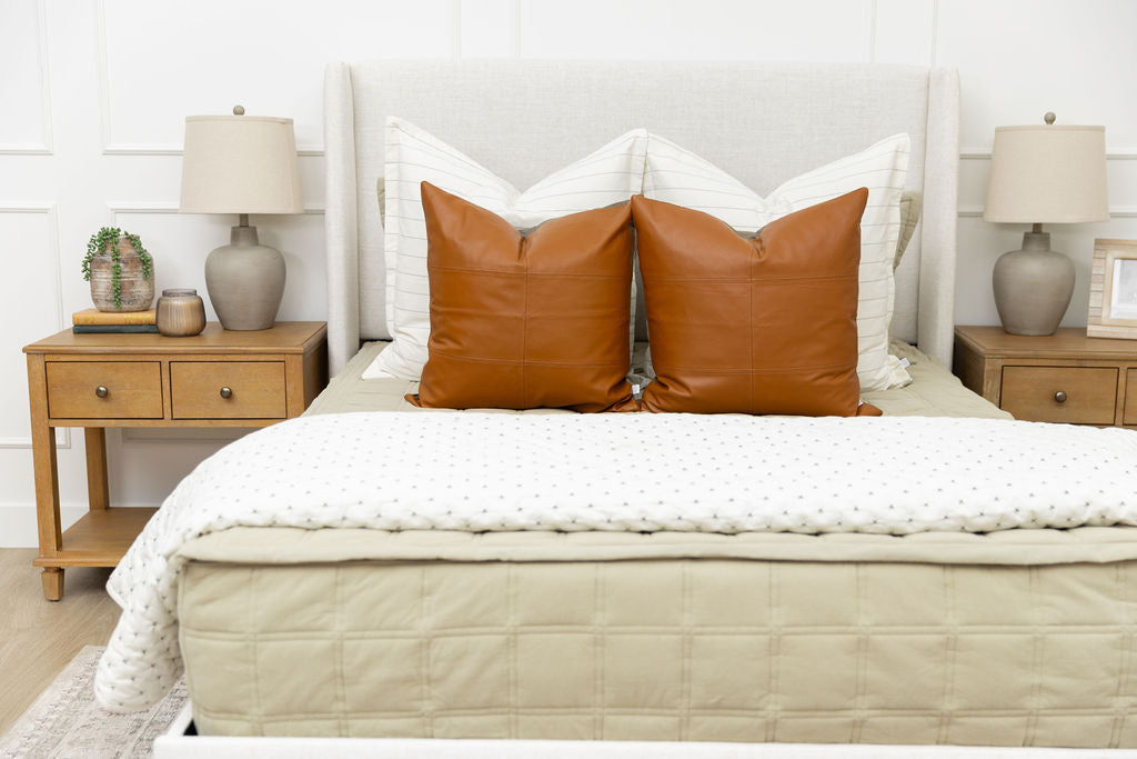 A bed made with khaki zipper bedding and an assortment of cream and leather bedding accessories.