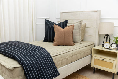 A twin bed made with khaki green zipper bedding and an assortment of black striped and brown pillows and blanket.