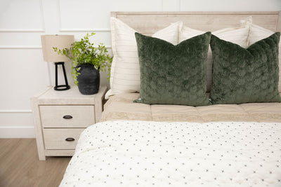 A bed made with tan zipper bedding and an assortment of neutral and green velvet throw pillows and blanket.