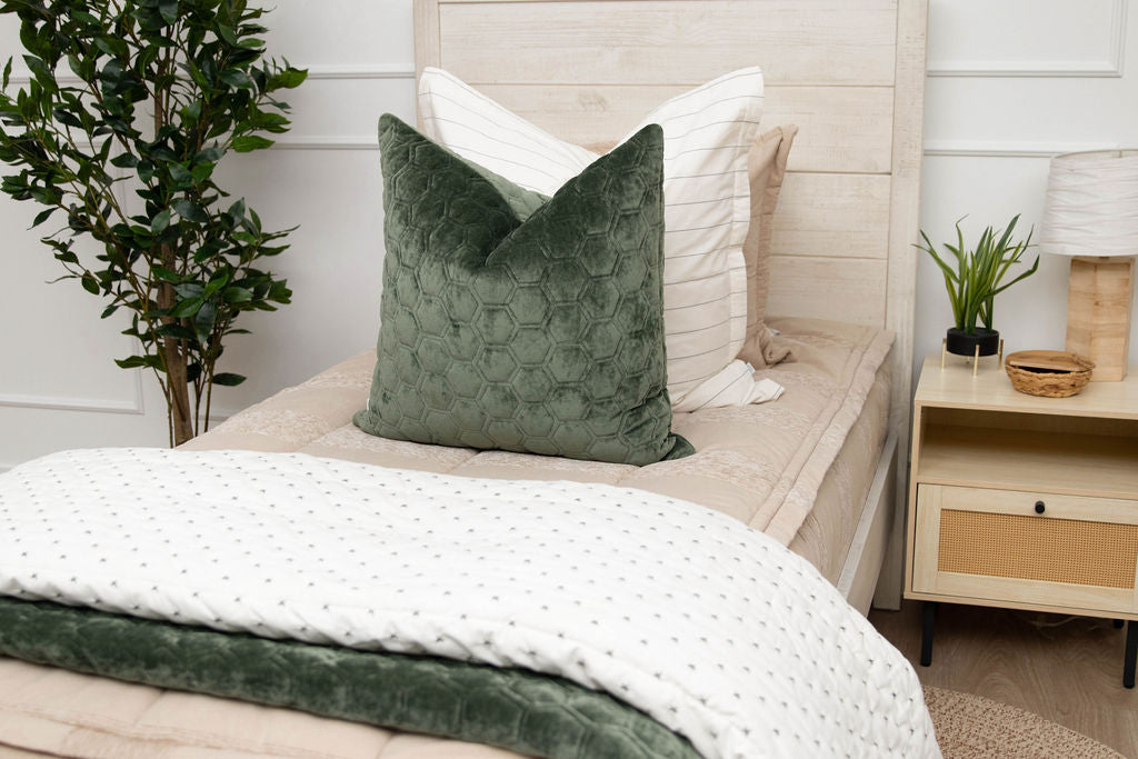 A twin bed made with tan zipper bedding and neutral and velvet green pillows and blankets.