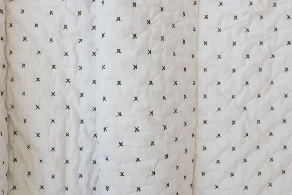 A close up of a creamy white blanket exterior with green "x" stitching.