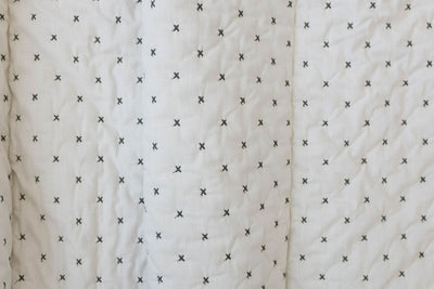A close up of a creamy white blanket exterior with green "x" stitching.