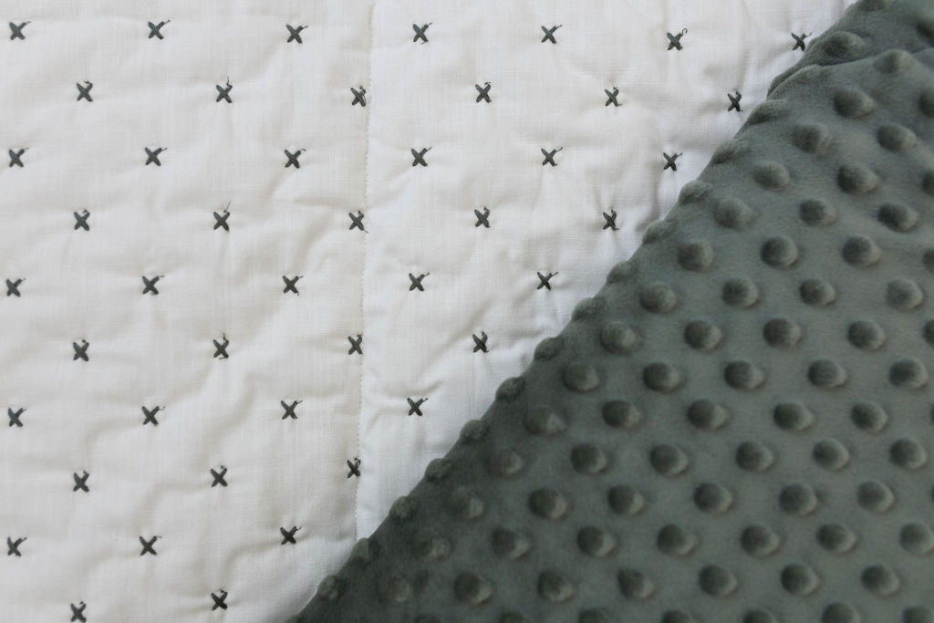 A close up of a creamy white blanket exterior with green "x" stitching and it folded over to reveal the green minky interior.