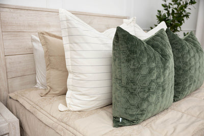 A close up view of a bed made with tan zipper bedding and neutral and velvet green pillows.
