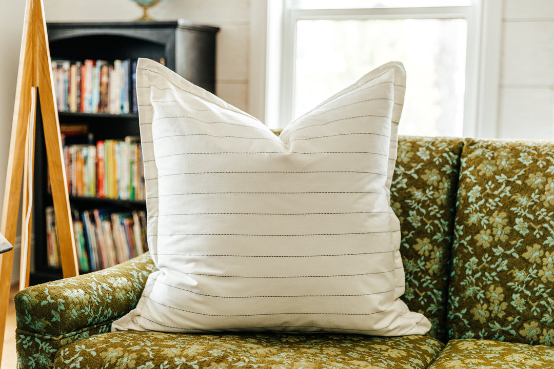 A cream XL euro pillow with green stripes arranged on a floral green couch. 
