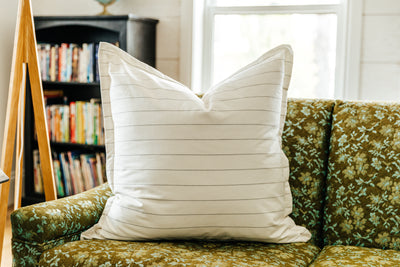 A cream XL euro pillow with green stripes arranged on a floral green couch. 