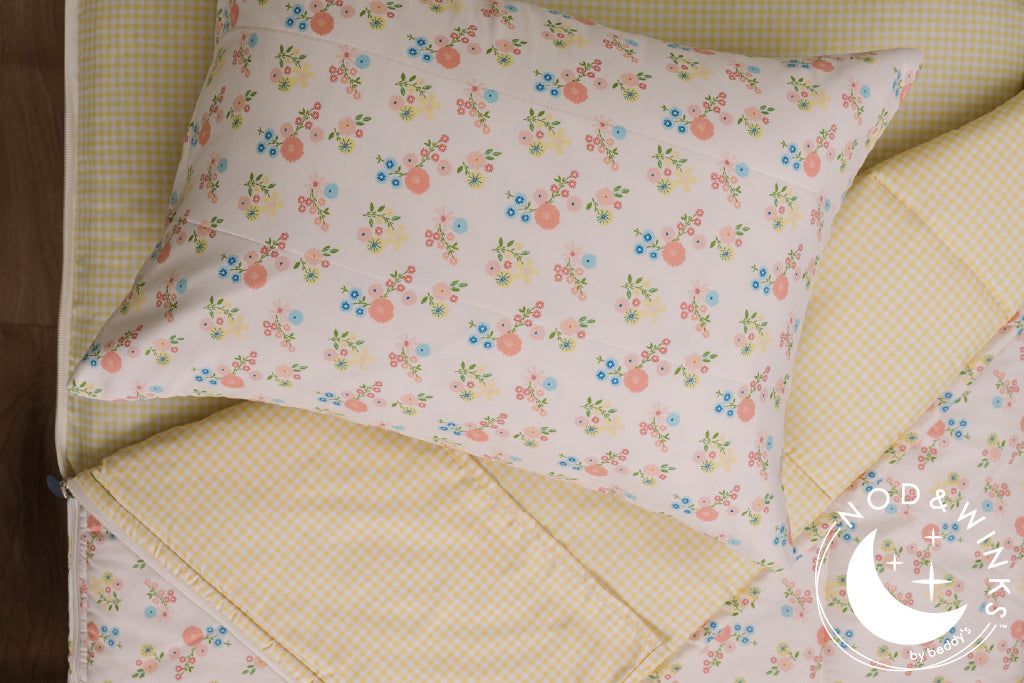 Yellow gingham and flower printed kids zipper bedding with the top unzipped and one side pulled back to reveal the inside lining, the pillow tossed on top of the bed.