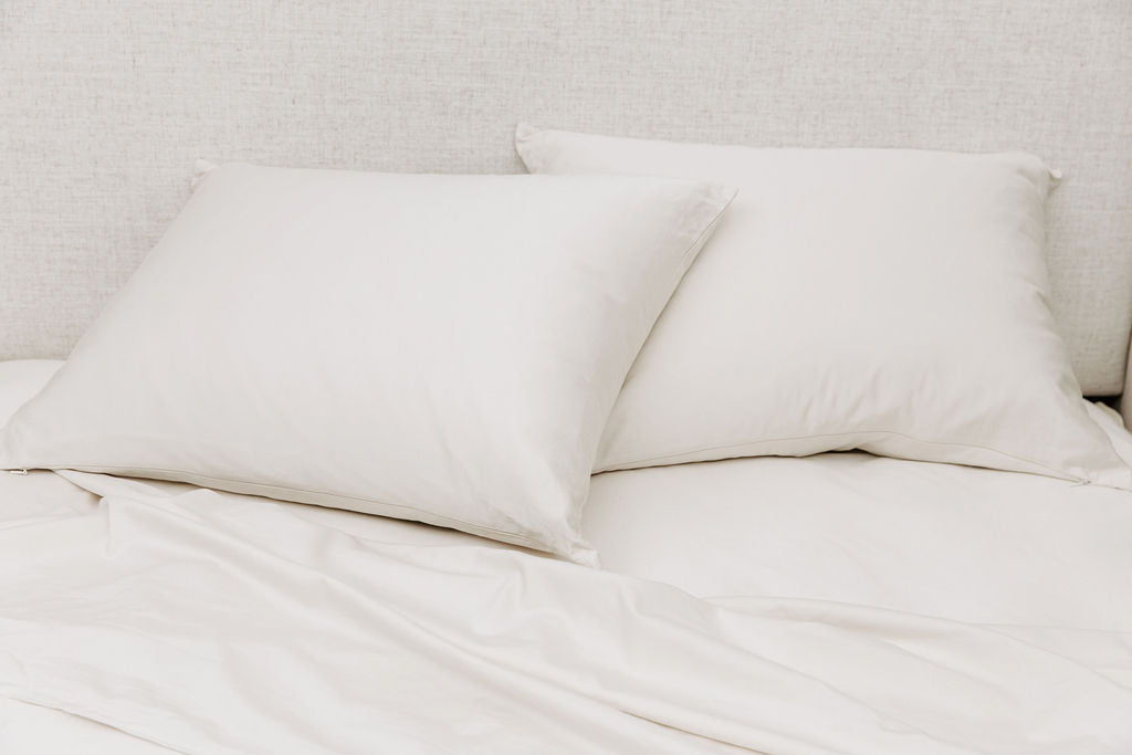 A bed made with white zipper sheets with the top sheet pulled back and pillows on top of the bed.