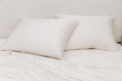 A bed made with white zipper sheets with the top sheet pulled back and pillows on top of the bed.