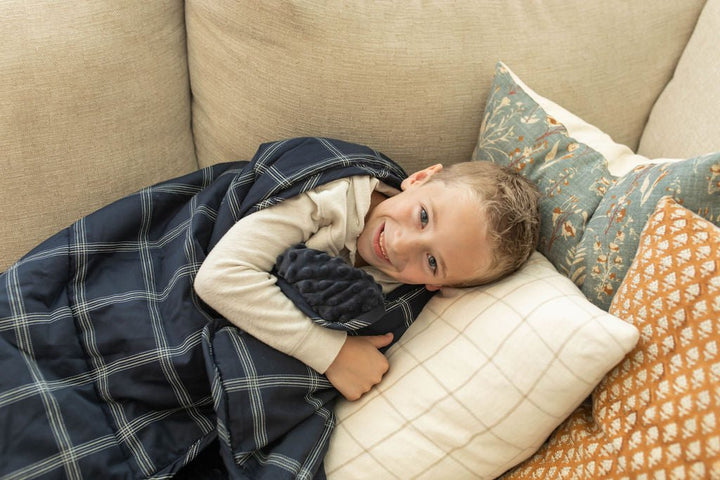 Child smiling on couch cuddling blue mini blanket