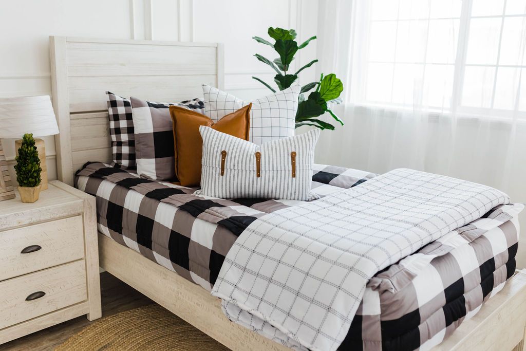 twin bed with Black and white buffalo plaid bedding with white and black grid euro, faux leather pillows, white and black striped lumbar with faux lather buckles and white and black grid pattered blanket