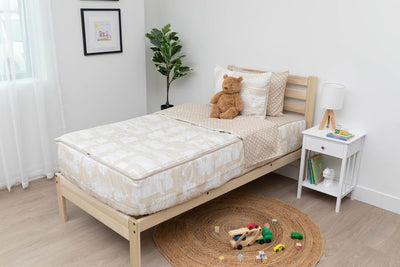 A twin bed made with light tan cars kids zipper bedding, a nightstand beside it with books on the shelf and toys scattered on the floor.