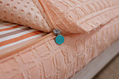photo showing zipper edge on peach bedding with textured rectangle design, white and orange stripe sheet and peach minky interior