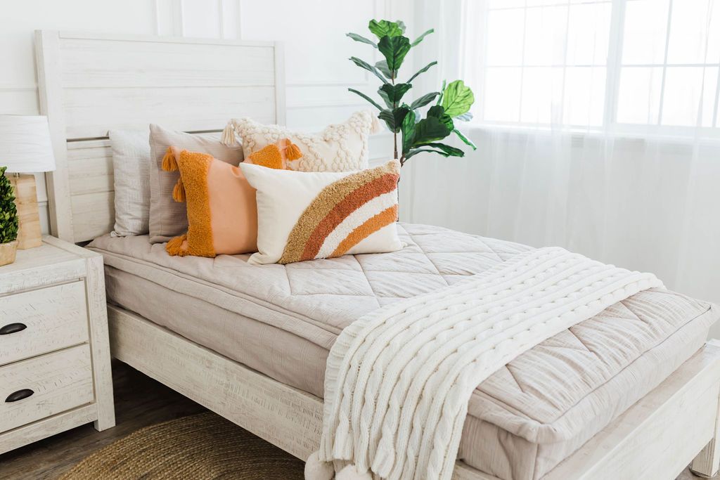 twin bed with Tan textured zipper bedding dark cream textured euro, orange, textured pillow with tassels, rainbow lumbar and knitted chenille throw with pom poms