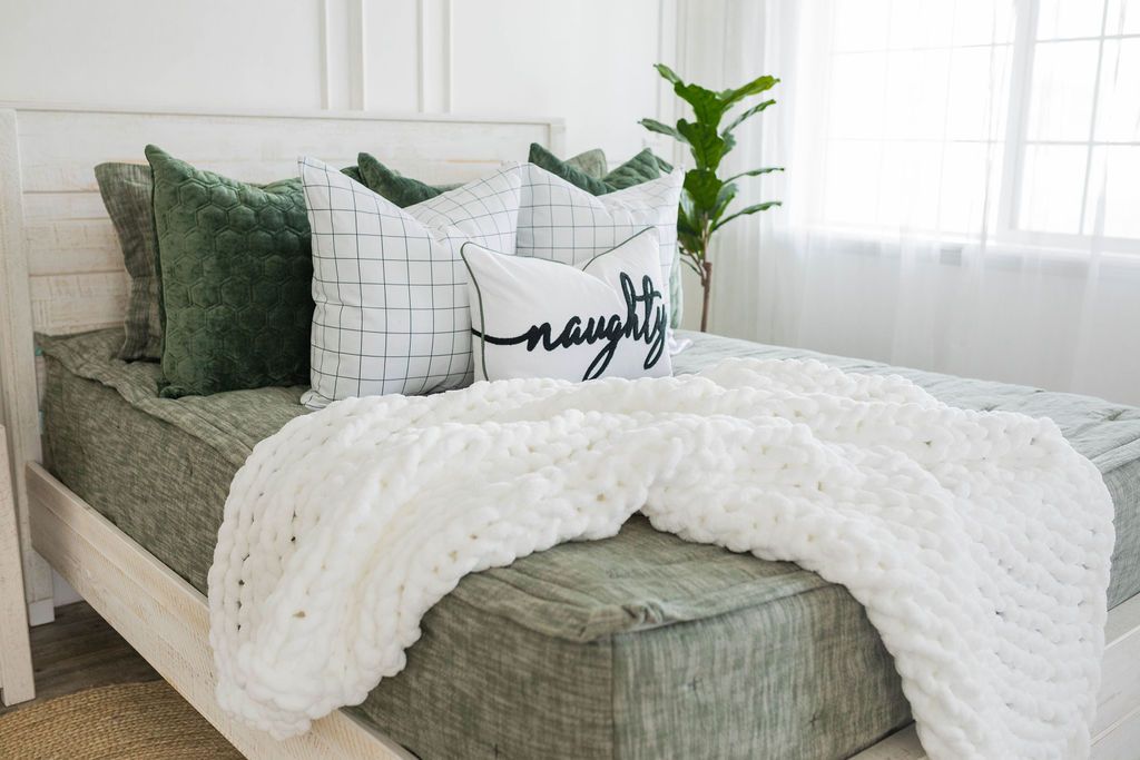 White pillow with black text spelling 'naughty' on green zipper bedding with green and white pillows and white throw blanket