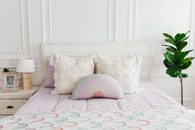 White queen bedframe purple textured zipper bedding and textured euro pillow with tassels, pastel rainbow pillow, and a white blanket with ombre purple, orange and green rainbows