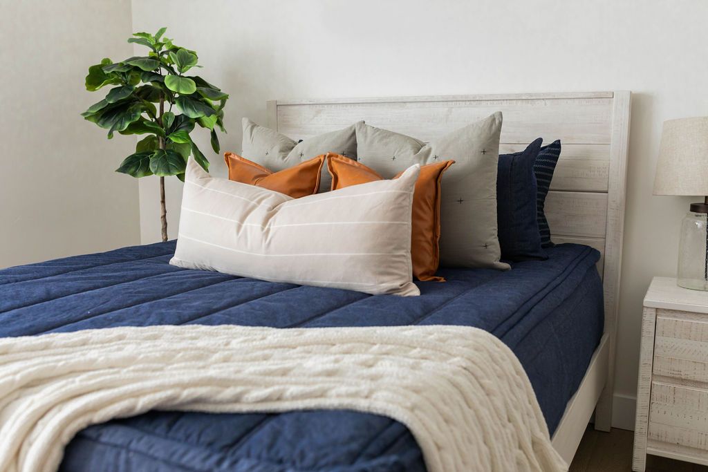 Dark blue zipper bedding with matching pillow cases and shams. Decorated with cream pillow and lumbar pillow, brown leather pillows, and cream throw blanket