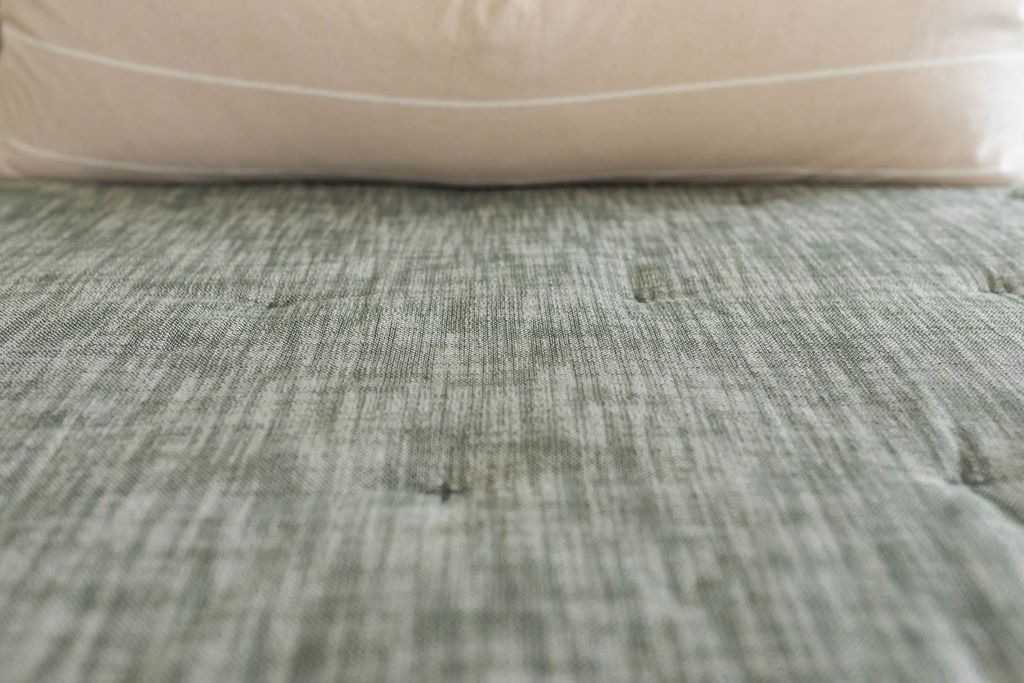 Close up view of texture of Green zipper bedding with cream lumbar pillow
