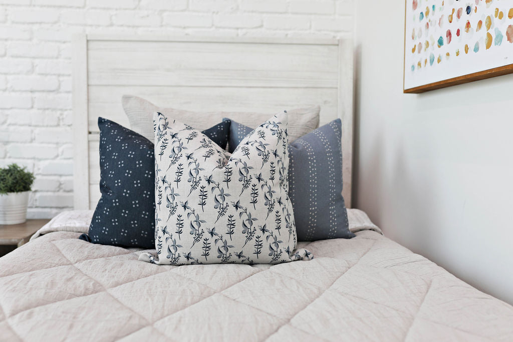 tan textured bedding and dark blue pillow with dotted flower pattern, light blue pillow with dotted lines, gray pillow with blue floral pattern