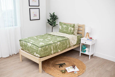 A twin bed made with olive green dinosaur fossils kids zipper bedding, a nightstand beside it with books on the shelf and toys scattered on the floor.
