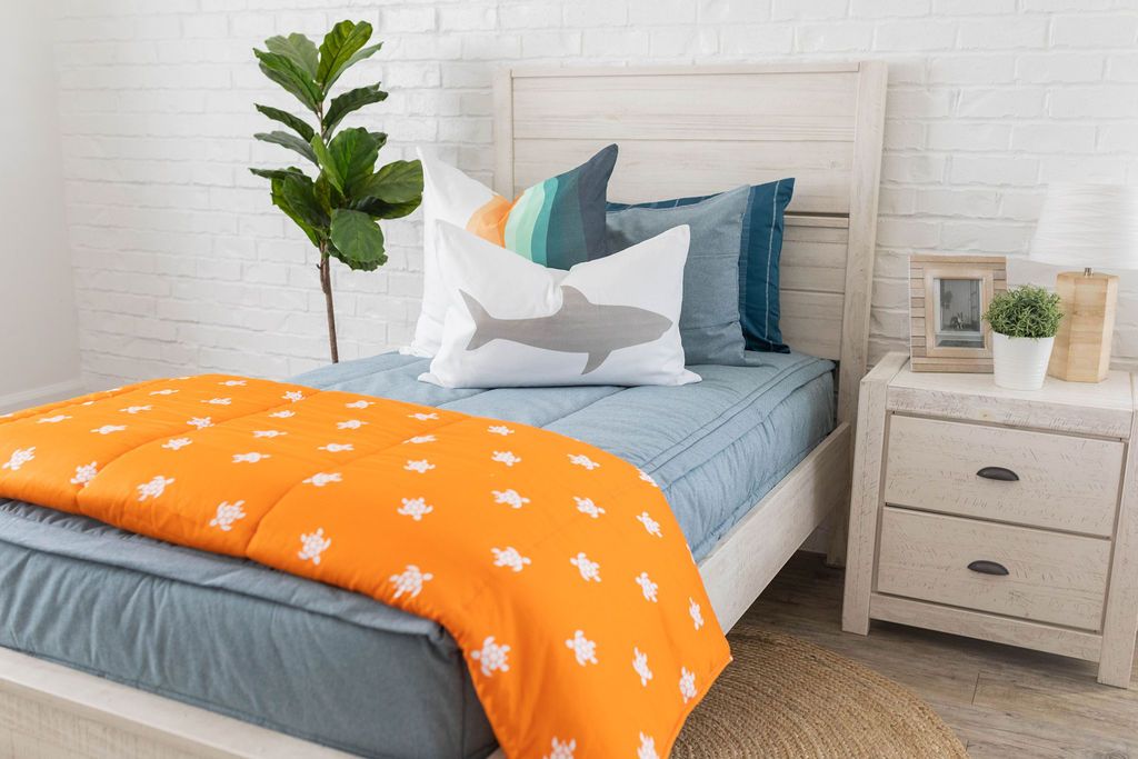 Light blue zipper bedding with matching sham and dark blue pillow case. Decorated with shark graphic pillow and orange blanket