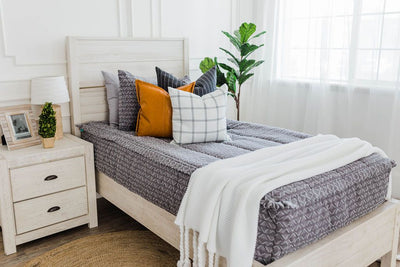 twin bed with Gray bedding with textured diamond design with deep navy striped euros, faux leather pillows, white and black grid pillow, and white textured blanket with braided tassels