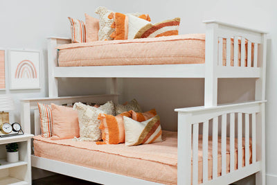 bunk bed with Peach bedding with textured rectangle design with dark cream textured euro, orange, textured pillow with tassels, rainbow lumbar and knitted chenille throw with pom poms