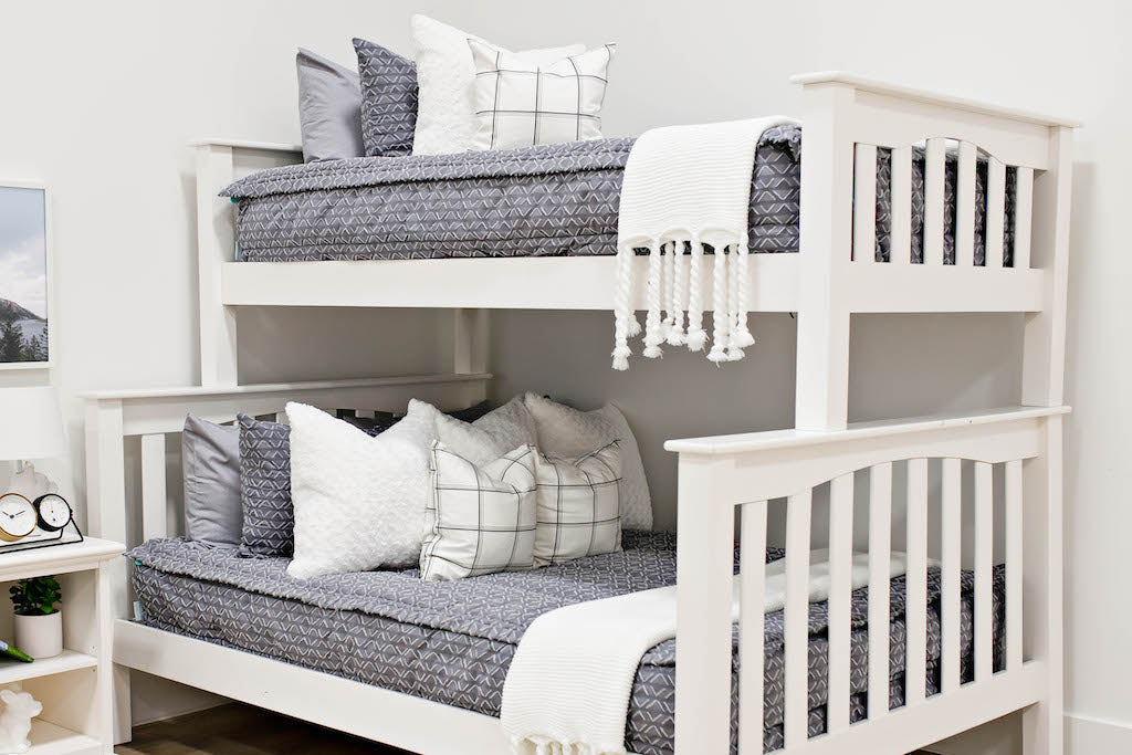 bunk bed with Gray bedding with textured diamond pattern and white faux fur textured euro, white and gray plaid pillow and white knitted throw with braided tassels at the foot of the bed