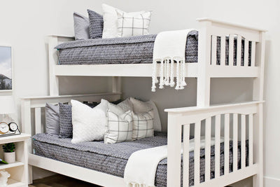 bunk bed with Gray bedding with textured diamond pattern and white faux fur textured euro, white and gray plaid pillow and white knitted throw with braided tassels at the foot of the bed