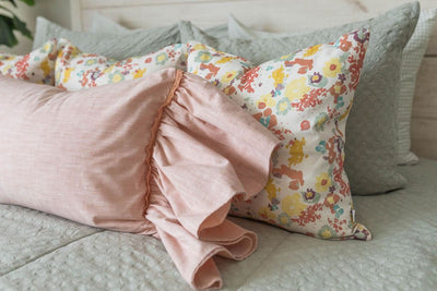 A close up side view of a bed made with textured sage green zipper bedding and multi-color floral and pink pillows.