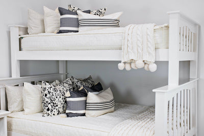 bunk bed with Cream bedding with textured rectangle design and cow rawhide print euro, black and cream stiped pillow, cream and black striped lumbar, cream knitted chenille throw with pom poms