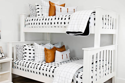 bunk bed with White bedding with black dashed lines and white and black grid euro, faux leather pillows, white and black striped lumbar with faux lather buckles and white and black grid pattered blanket
