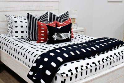 queen bed with White bedding with black dashed lines black and white striped euros, red and white dashed pillow, black lumbar with white longboard print and black blanket with white dashed lines
