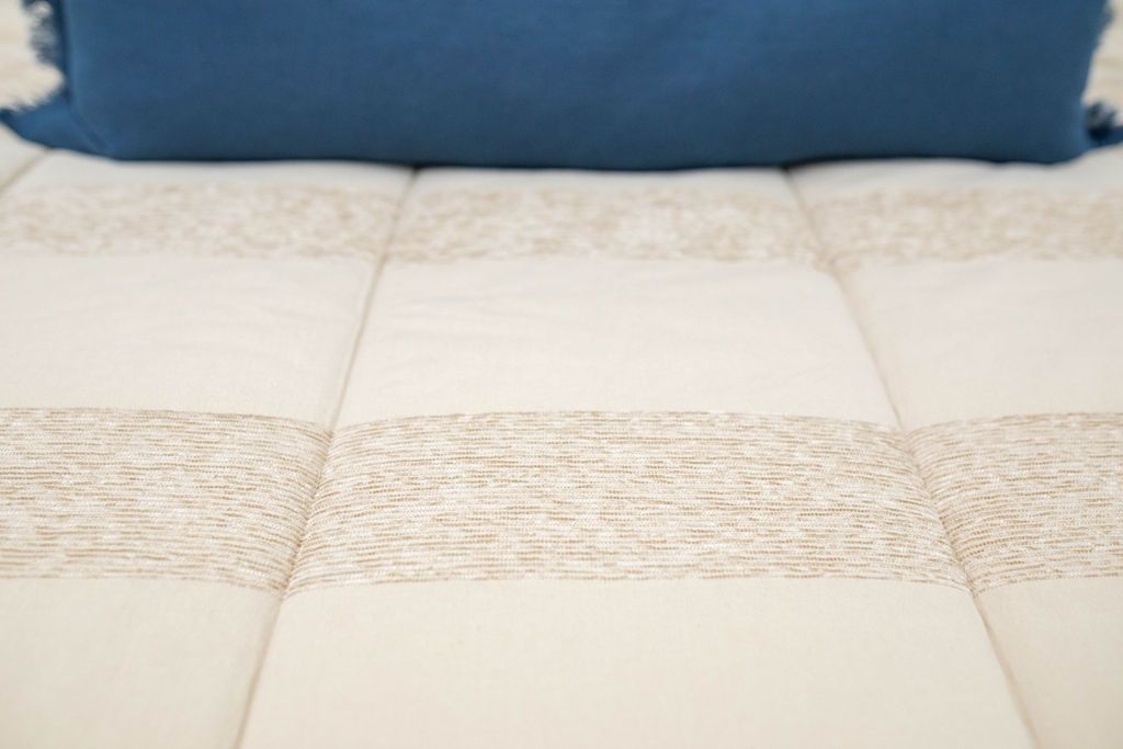 Close up of tan zipper bedding showing texture. Bedding styled with blue lumbar pillow