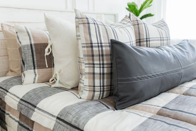 A close up view of a bed made with tan, charcoal gray, and cream plaid design zipper bedding with neutral cream, plaid pattern, and leather pillows.