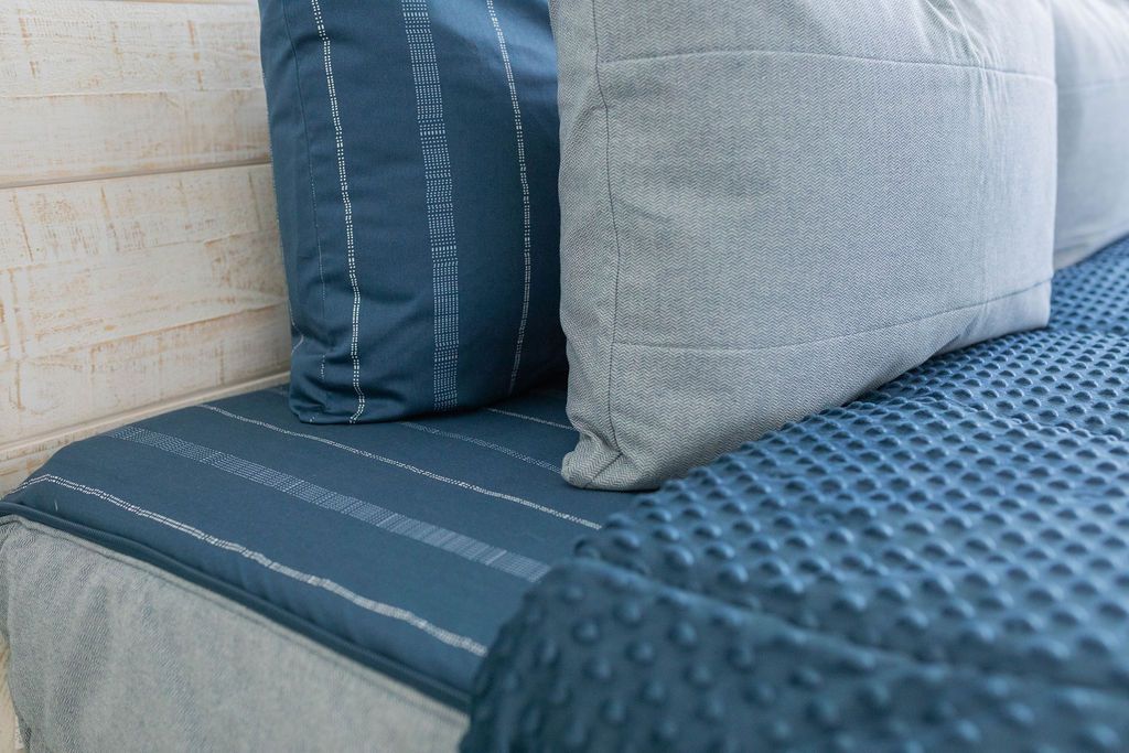Dark and light blue pillows on a matching blue zipper bedding with the comforter pulled back. 