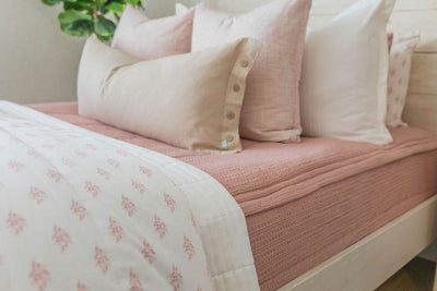 Side view of pink zipper bedding decorated with white and pink pillowcases and shams. Cream lumbar pillow and white blanket