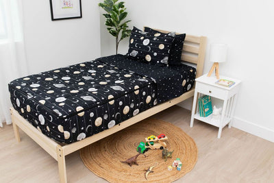 A twin bed made with black planets and stars kids zipper bedding, a nightstand beside it with books on the shelf and toys scattered on the floor.