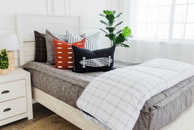 twin bed with Brown and gray woven textured bedding black and white striped euros, red and white dashed pillow, black lumbar with white longboard print and white and white and black grid blanket