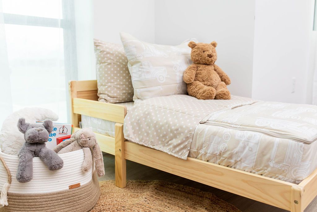 A toddler bed made with light tan cars kids zipper bedding and a basket of stuffed animals beside it.