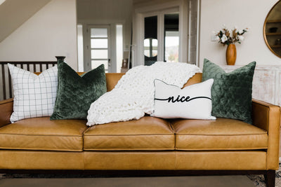 White and fluffy chain woven blanket on tan leather couch with green and white pillows