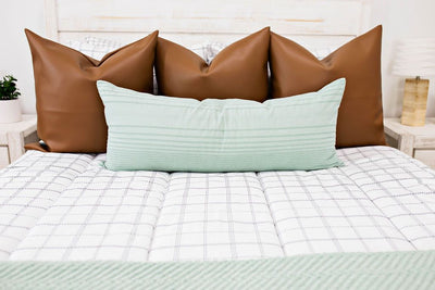 Brown faux leather pillows on white zipper bedding with teal lumbar pillow and throw blanket