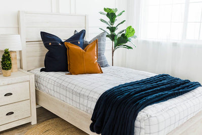 White and black grid patterned bedding with blue stitched grid euro, denim euro with buttons, faux leather pillow, and navy chenille knitted throw