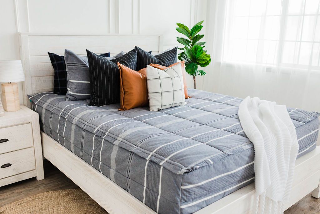 Queen bed with Deep navy woven stripe bedding with deep navy striped euros, faux leather pillows, white and black grid pillow, and white textured blanket with braided tassels