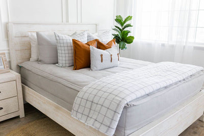 Light gray zipper bedding with white and gray pillowcases and shams. Decorated with brown leather pillow, stripped white pillows and matching blanket