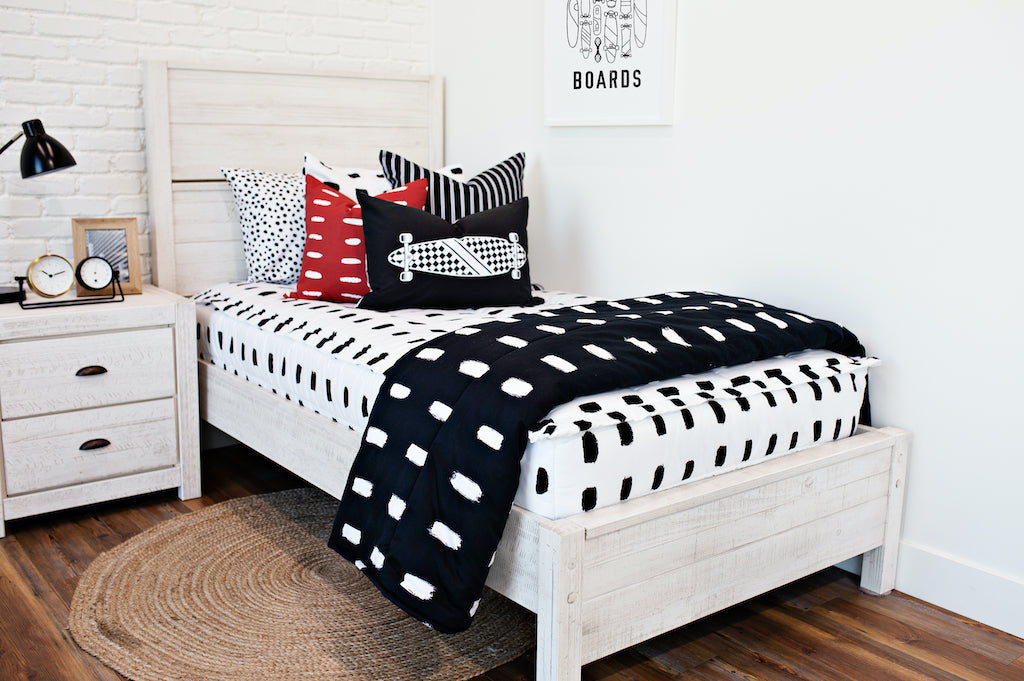 twin bed with white and black dashed bedding and White and black striped euro, red and white dashed pillow, black lumbar with white longboard print, black blanket with white dashed lines at the foot of the bed